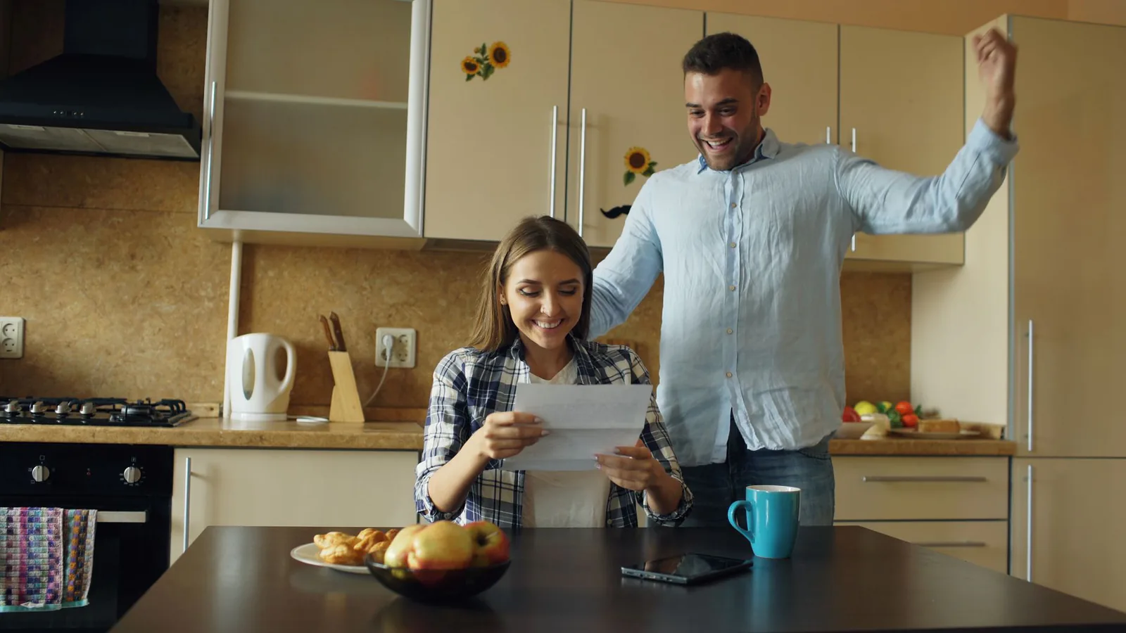 A joyful couple in a cozy kitchen celebrating good news received in the mail
